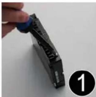 Close-up of a hand holding a blue plastic clip next to a black mechanical component, with a numbered circle marker (1) in the corner.
