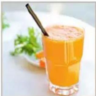 Glass of orange-colored juice with a straw, garnished with fresh green vegetables (no text or symbols visible)