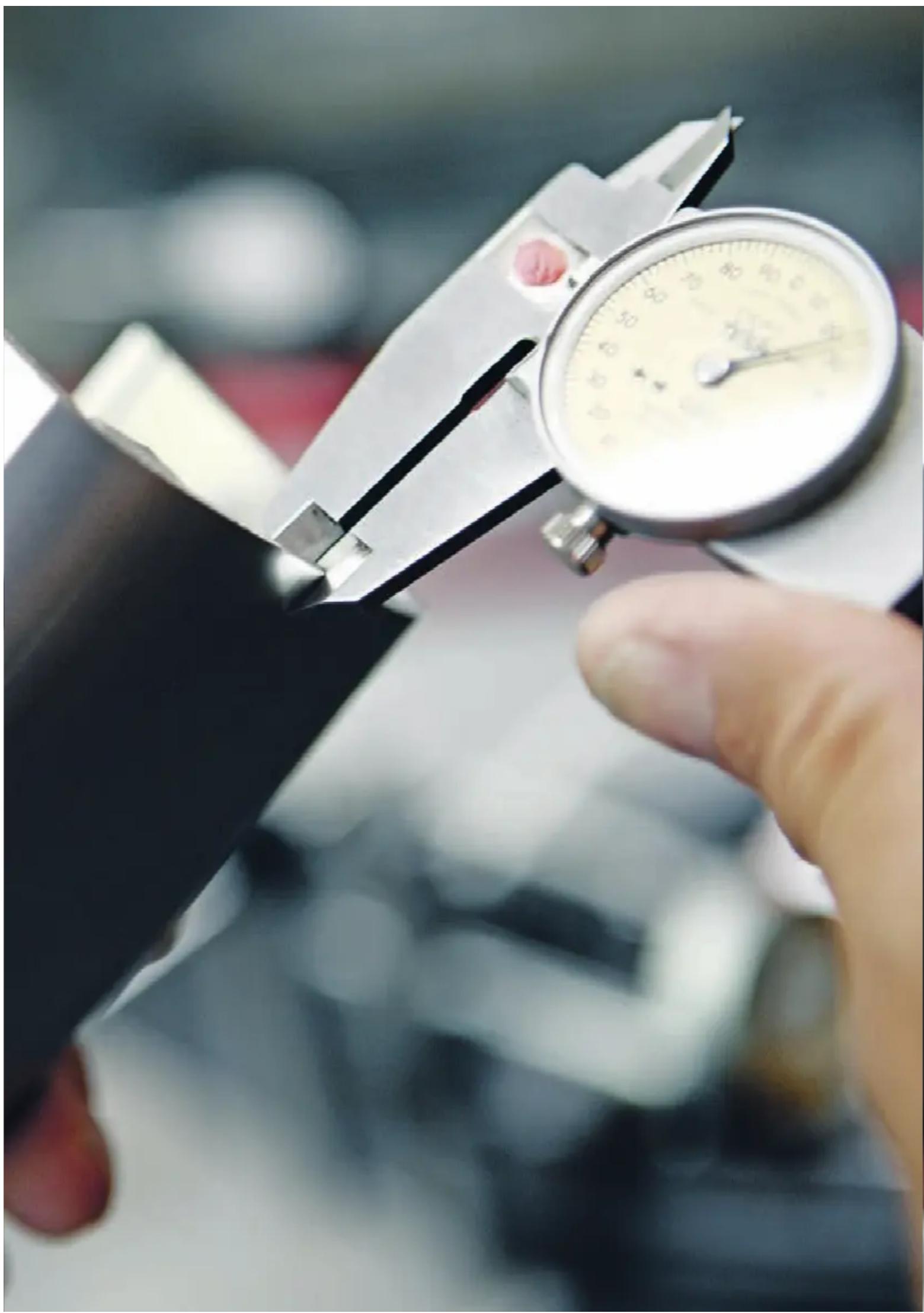 Close-up of a hand using a vernier caliper to measure a metric, no visible text or symbols on the instrument itself.