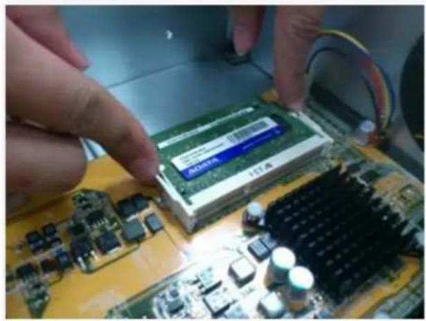 Close-up of hands installing a green RAM module on a computer motherboard (no visible text or symbols)
