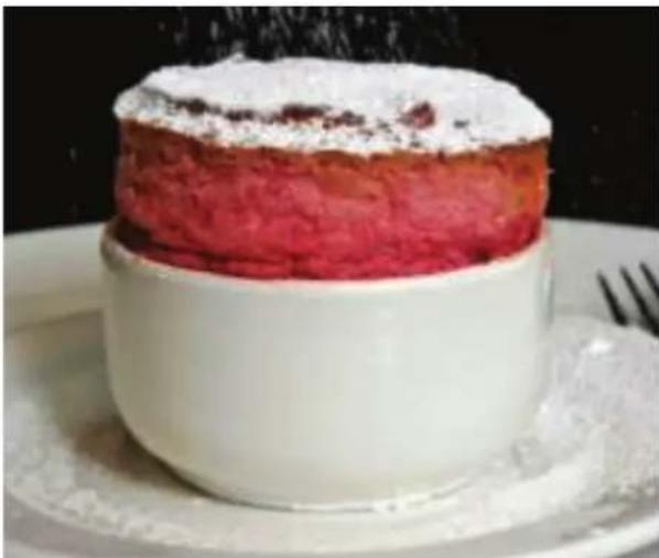 Close-up of a layered dessert with pink topping and white cup, placed on a white plate (no text or symbols visible)