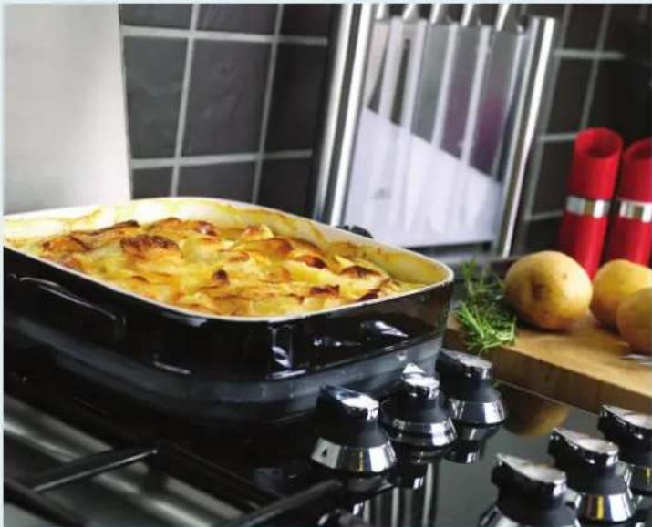 Exterior view of a modern kitchen with a large rectangular dish on a gas stove, surrounded by potatoes and herbs (no signage or text visible)