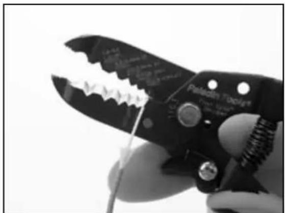 Close-up of a hand using a Pilgrim Toolbox to cut a wire (no visible text or symbols)