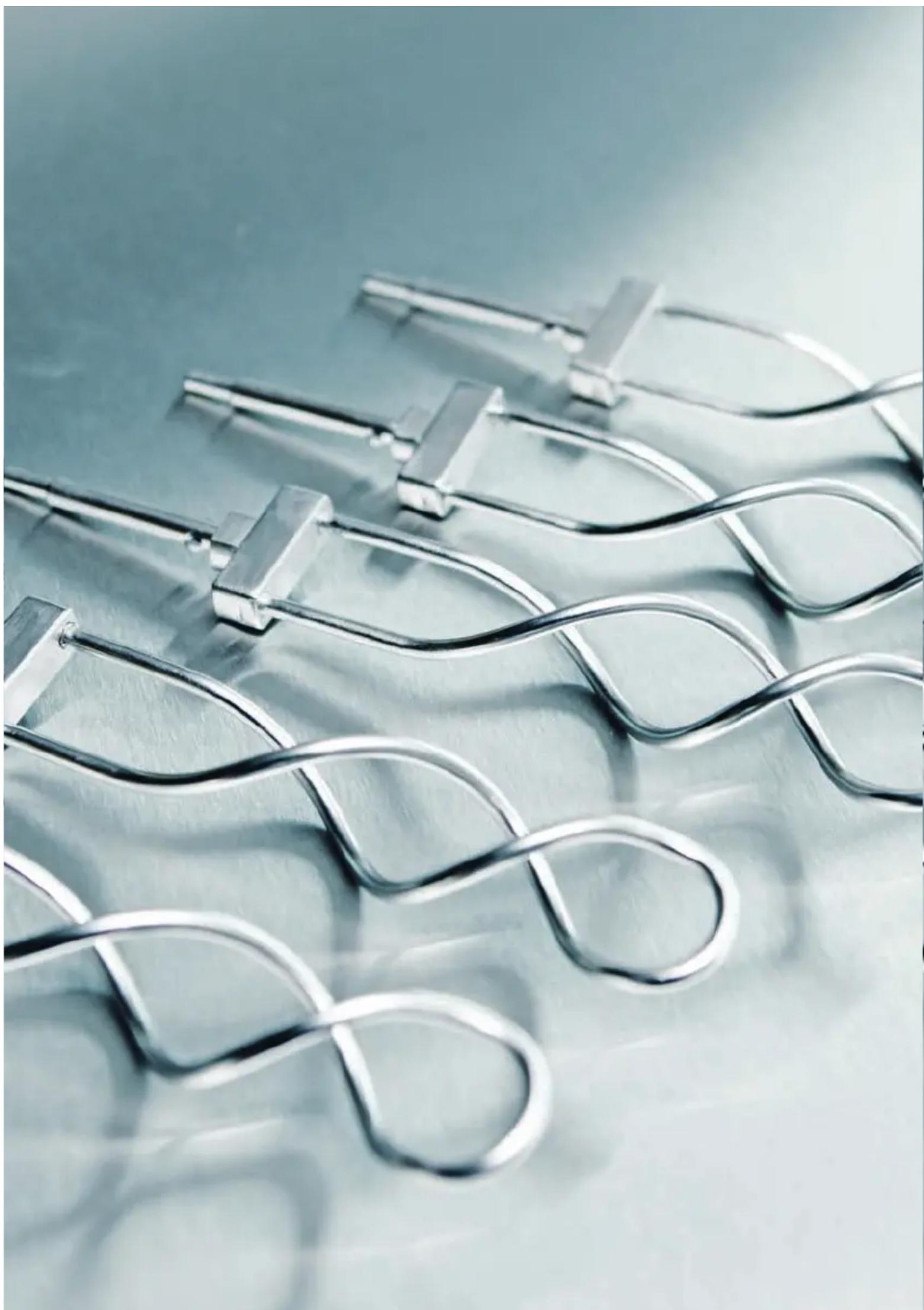 Close-up of metallic wire clips arranged in a wavy pattern on a reflective surface (no text or symbols visible)