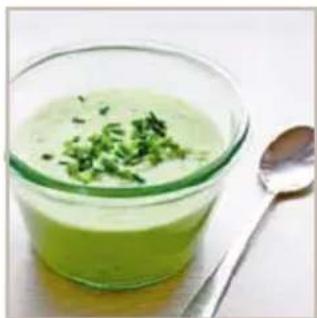 Glass bowl containing a green creamy mixture with chopped green herbs, accompanied by a spoon (no text or symbols visible)