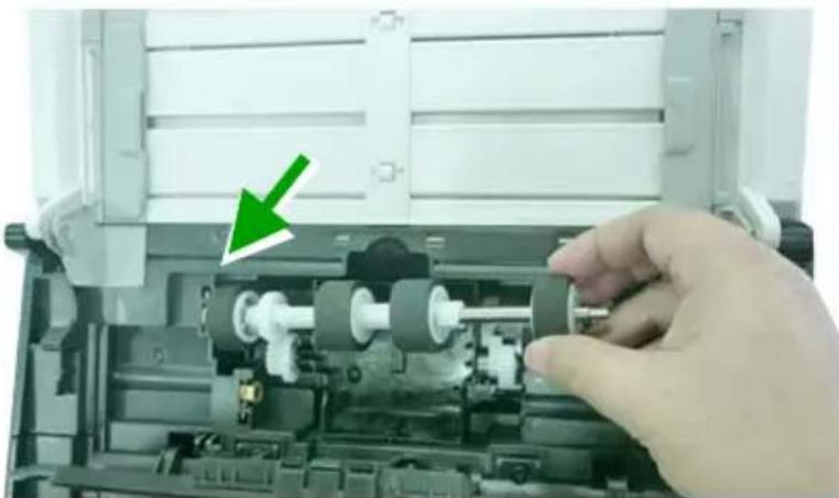 Close-up of a hand inserting a component into a mechanical device, with a green arrow pointing to the component (no text or symbols visible)