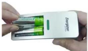 Close-up of hands holding a white electronic device with green batteries and a green charging plug (no visible text or symbols)