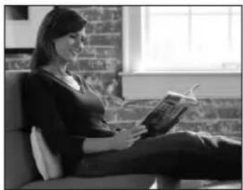 Black-and-white photo of a woman sitting on a couch reading a book, with brick wall background (no visible text or symbols)