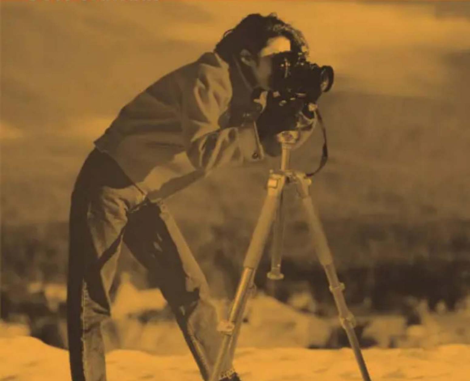 Person using a camera on a tripod in a snowy landscape (no visible text or symbols)