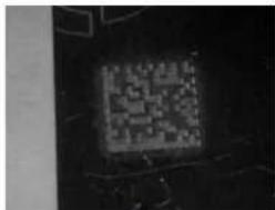 Black-and-white image showing a pixelated QR code on a dark background, likely for scanning or data processing purposes.