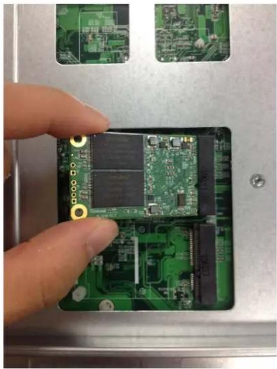 Close-up of a hand holding a green printed circuit board with gold contacts, placed on a metal tray (no visible text or symbols)