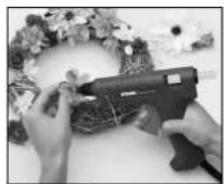 Close-up of hands arranging a decorative floral wreath with a black tool (no visible text or symbols)
