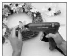 Close-up of hands using a handheld tool to spread fabric around a floral wreath (no visible text or symbols)