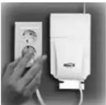 Hand inserting a plug into an electrical outlet wall, next to a white appliance mounted on a wall (no visible text or symbols)