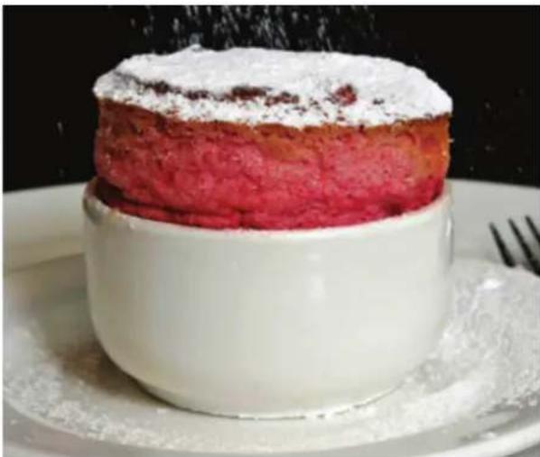 Close-up of a layered dessert with white frosting and powdered sugar, placed on a white plate (no text or symbols visible)