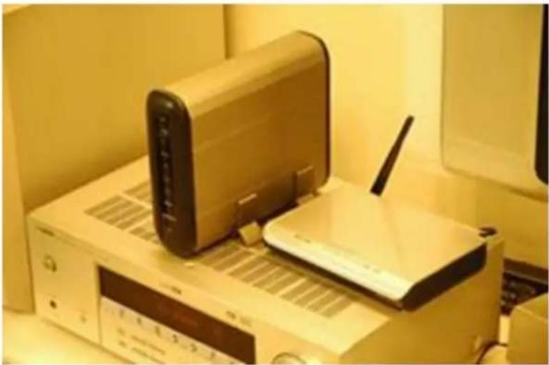 Exterior view of a beige electronic device with a beige router and antenna, placed on a white base (no visible text or symbols)