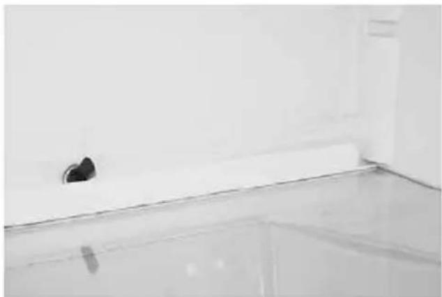 Interior corner of a room with a white tiled wall and a small black circular object on the floor (no text or symbols visible)