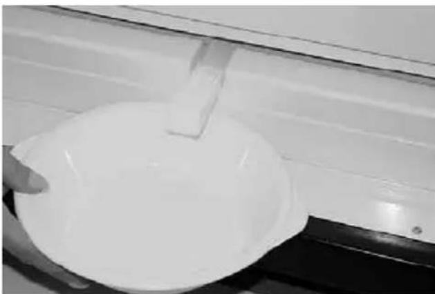 Close-up of a white bowl with a small object above it, placed on a dark surface near a window (no visible text or symbols)