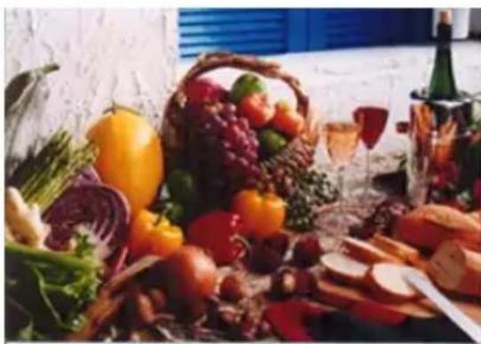 Assorted fresh fruits and vegetables arranged on a table, including a basket of grapes, bell peppers, and wine bottle (no visible text or labels)