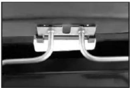 Close-up of a white cable or wire connector with two metal clips, mounted on a black surface (no text or symbols visible)