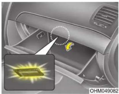 Interior view of a car showing a device with a highlighted yellow icon and an inset image of a yellow rectangular object (no text or symbols)
