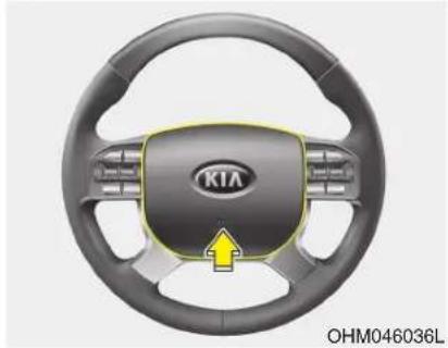 Close-up of a car steering wheel with the Kia logo and yellow arrow indicating clockwise motion (no text or symbols on the wheel itself)