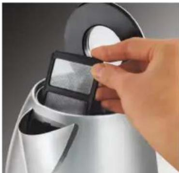 Hand placing a small object into a metallic kettle (no visible text or symbols)