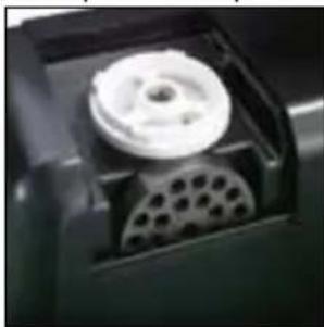 Close-up of a mechanical component with a white circular component and perforated base (no visible text or symbols)