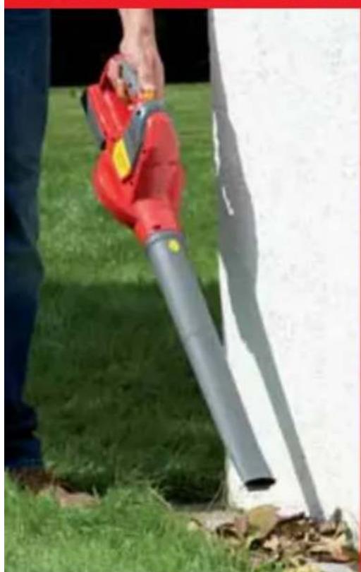 Person using a red and silver hair shaver on grass, next to a white wall (no text or symbols visible)