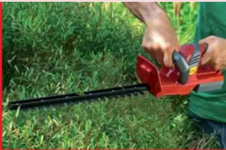 Person using a red-handled hatched shrub in a grassy field (no text or symbols visible)