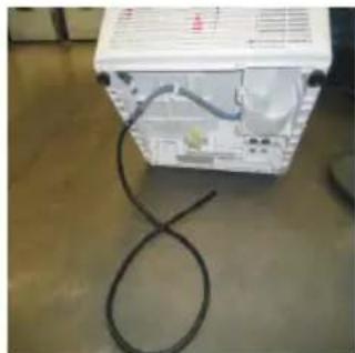 White electronic device with attached cables and wiring, placed on a concrete floor (no visible text or symbols)