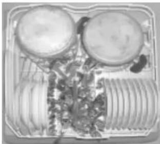 Top-down view of a food tray with two round containers and a side dish containing herbs (no visible text or labels)