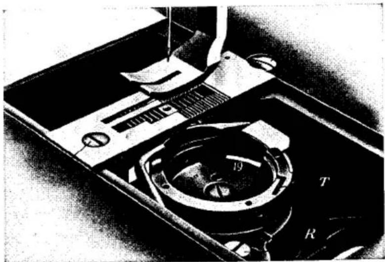 Gros plan d'un dispositif mécanique avec pièces étiquetées (D, T, R) et un outil, aucun texte ou symbole lisible au-delà des étiquettes.