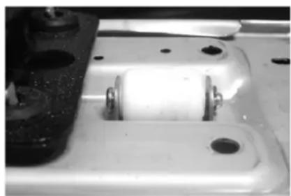 Close-up of a white mechanical component with two metallic clips and mounting holes (no visible text or symbols)