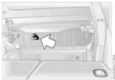 Interior view of a vehicle showing dashboard and engine compartment with a white arrow pointing to a component (no text or symbols visible)