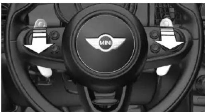 Interior view of a car dashboard with the Mini logo and directional arrows indicating steering wheel (no text or symbols beyond branding)