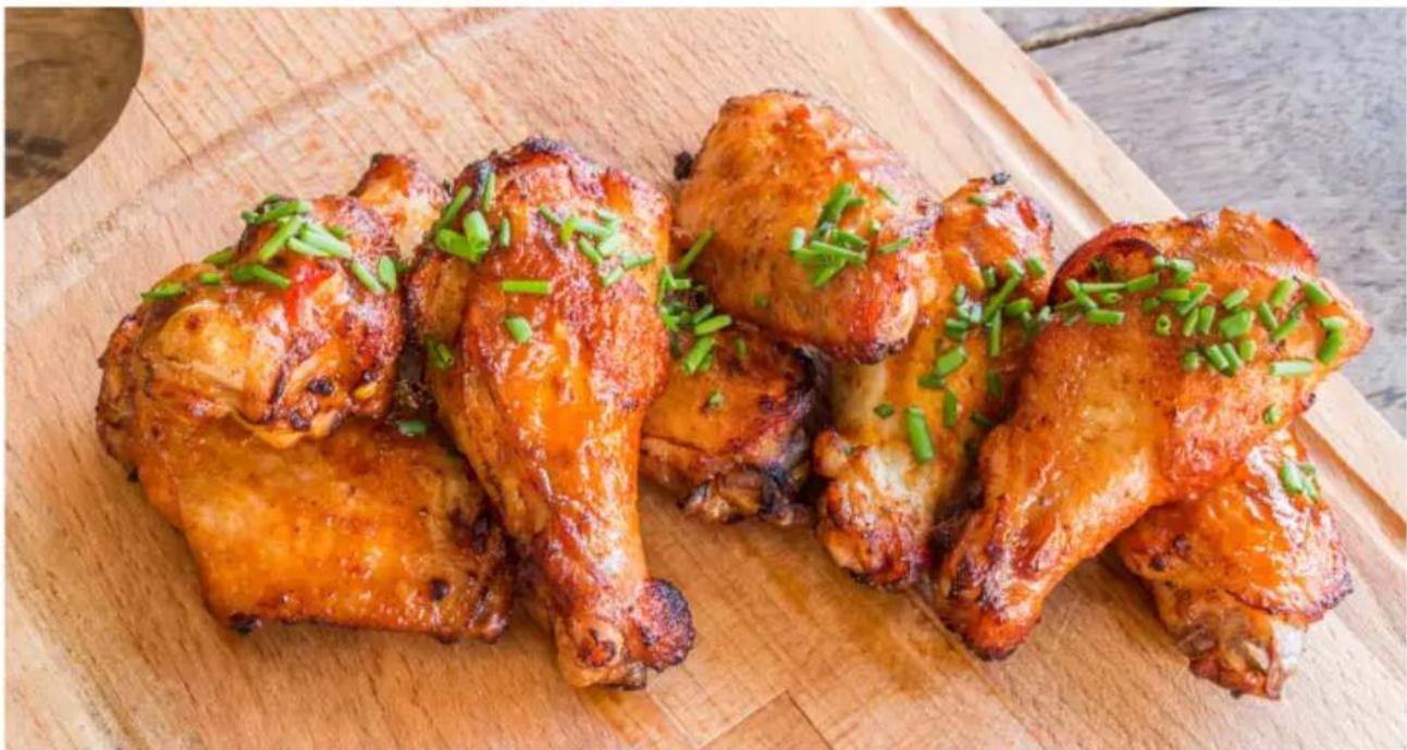Close-up of golden-brown fried chicken wings garnished with chopped green onions, served on a wooden cutting board (no text or symbols visible)