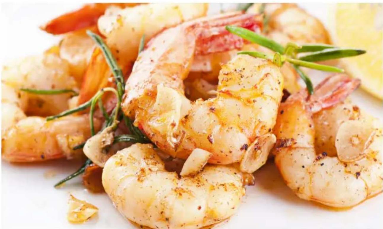 Close-up of golden-brown fried shrimp garnished with green herbs and a lemon slice (no text or symbols visible)