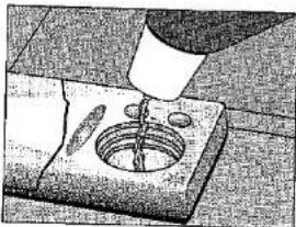 Close-up of a hand pouring liquid into a small container with a drain (no visible text or symbols)