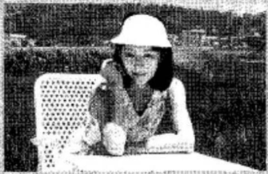 Photo en noir et blanc d'une personne assise à une table, portant un chapeau à large bord et une chemise à motifs (aucun texte ou symbole visible)