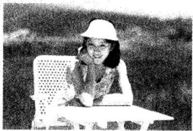 Photo en noir et blanc d'une personne assise à une table à l'extérieur, portant un chapeau (aucun texte ni symbole visible)