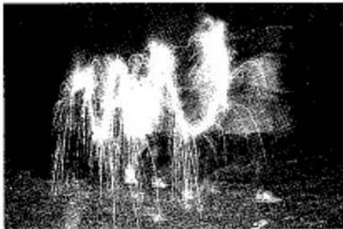 Photographie en noir et blanc d'une fontaine avec des jets d'eau et de la fumée s'élevant (aucun texte ou symbole visible).
