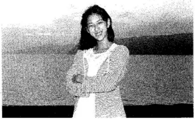Photo en noir et blanc d'une femme souriante les bras croisés, debout devant un fond uni (aucun texte ni symbole visible)