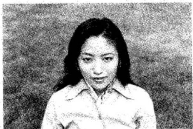 Portrait d'une femme aux cheveux mi-longs portant une chemise à col, bras croisés (pas de texte ni de symboles visibles)