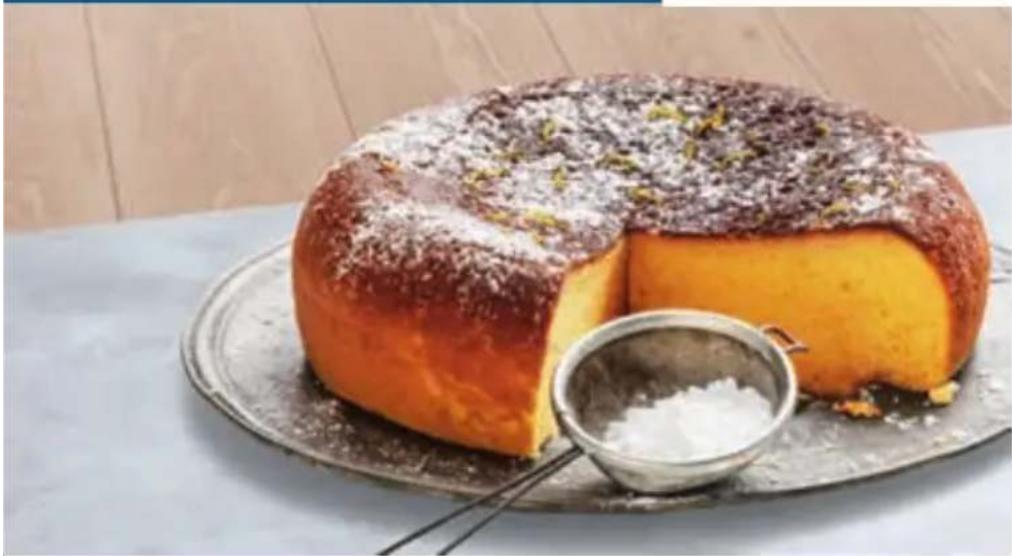 Close-up of a baked cake with powdered sugar topping and a small bowl of white powder on a metal plate (no text or symbols visible)