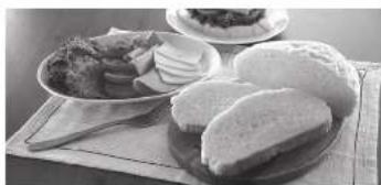 Black-and-white photo of a breakfast table with sliced bread, meat, and a bowl of food (no visible text or symbols)