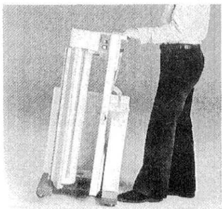 Personne debout à côté d'objets blancs empilés, peut-être une armoire ou un support (aucun texte ni symbole visible).