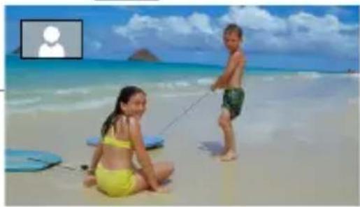 Two children on a sandy beach, one sitting on the floor and the other standing with a long pole, under a blue sky with clouds (no text or symbols visible)