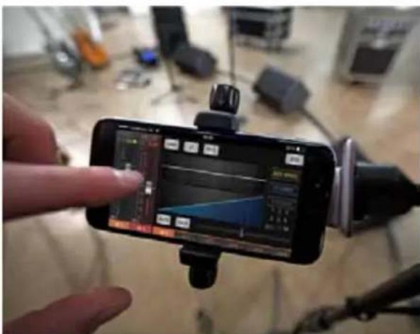 Hand holding smartphone displaying a game interface with a graph and timer, surrounded by other devices in the background.