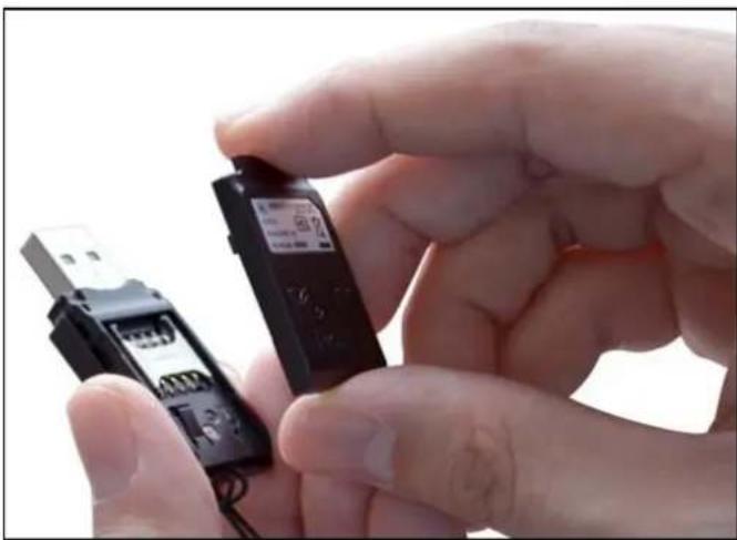 Close-up of a hand holding a black electronic device with a digital display, next to a small USB flash drive (no visible text or symbols)